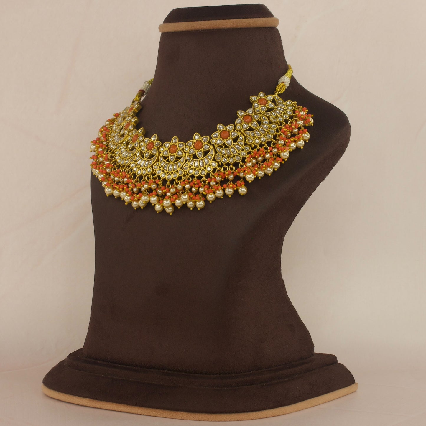 This is a Jadau Kundan Short necklace with flower designs. This is made in white jadau Kundan stones and coral stones. At the bottom of the necklace there are coral beads and pearls with 22k gold plating