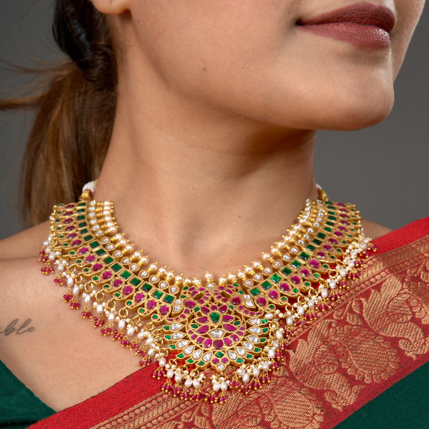 This is a Jadau Kundan short necklace with floral designs on it. This Neckpiece has ricepearls and ruby beads at bottom . This necklace is covered in 22k Gold plating