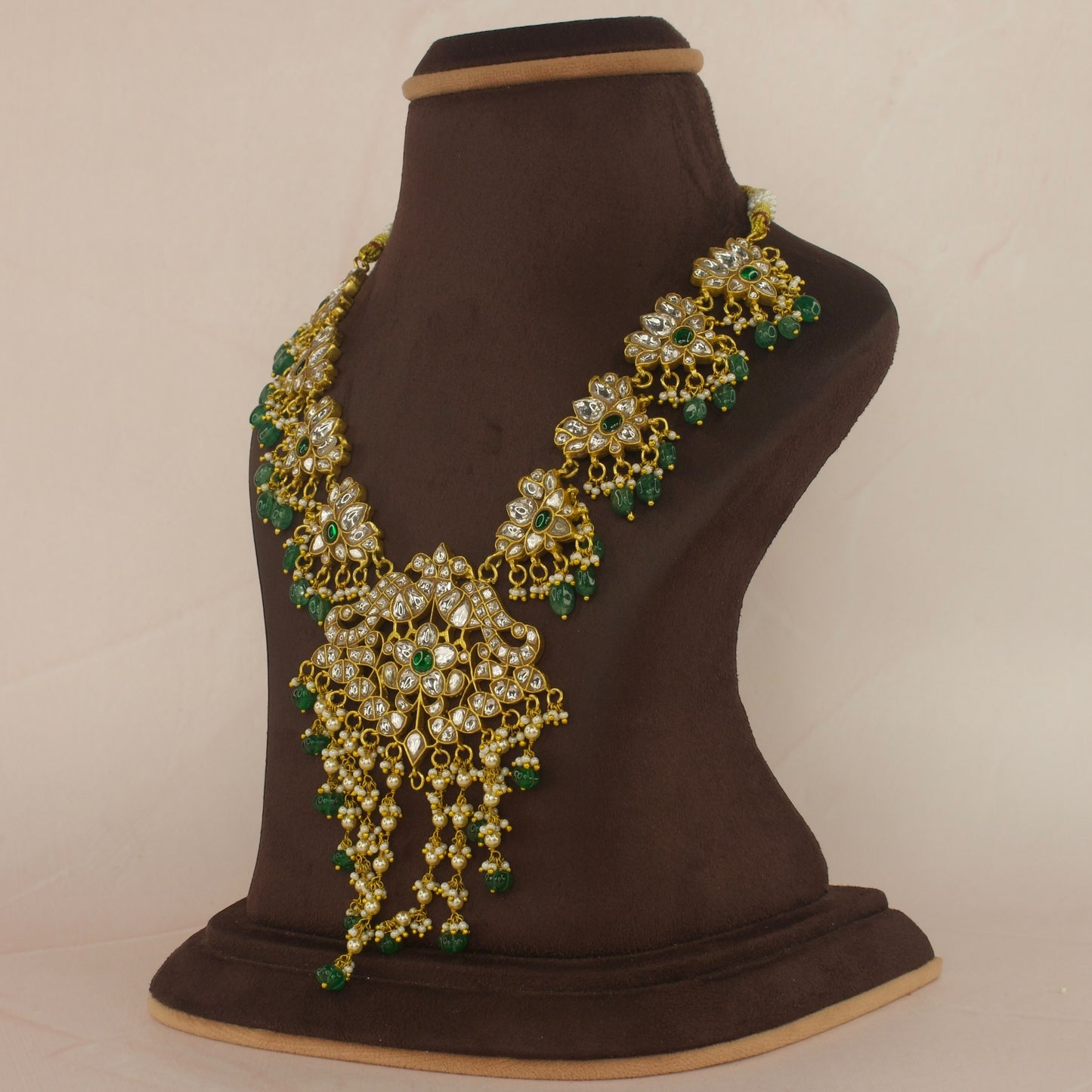 This is a Jadau Kundan Short Necklace, the Neckpiece has lotus designs all over it from the centre to the corners. This specific’s piece is with white Kundan stones and a singe green stone in the middle. The beads at bottom are Russian pumpkin beads.