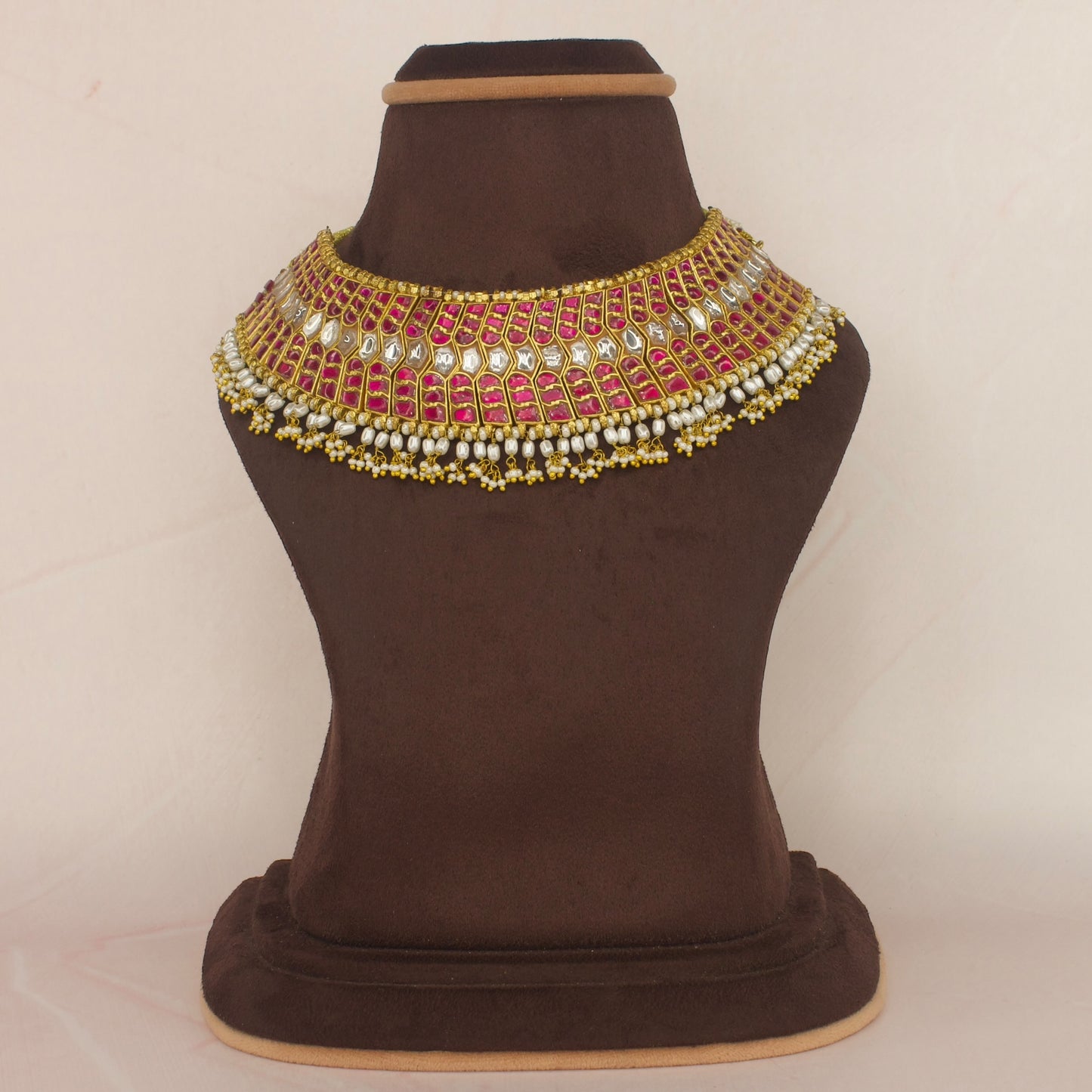 This is A jadau Kundan choker cum short necklace set in ruby stones. The piece is covered with 22k Gold plating and at the bottom of the piece we have Ricepearls