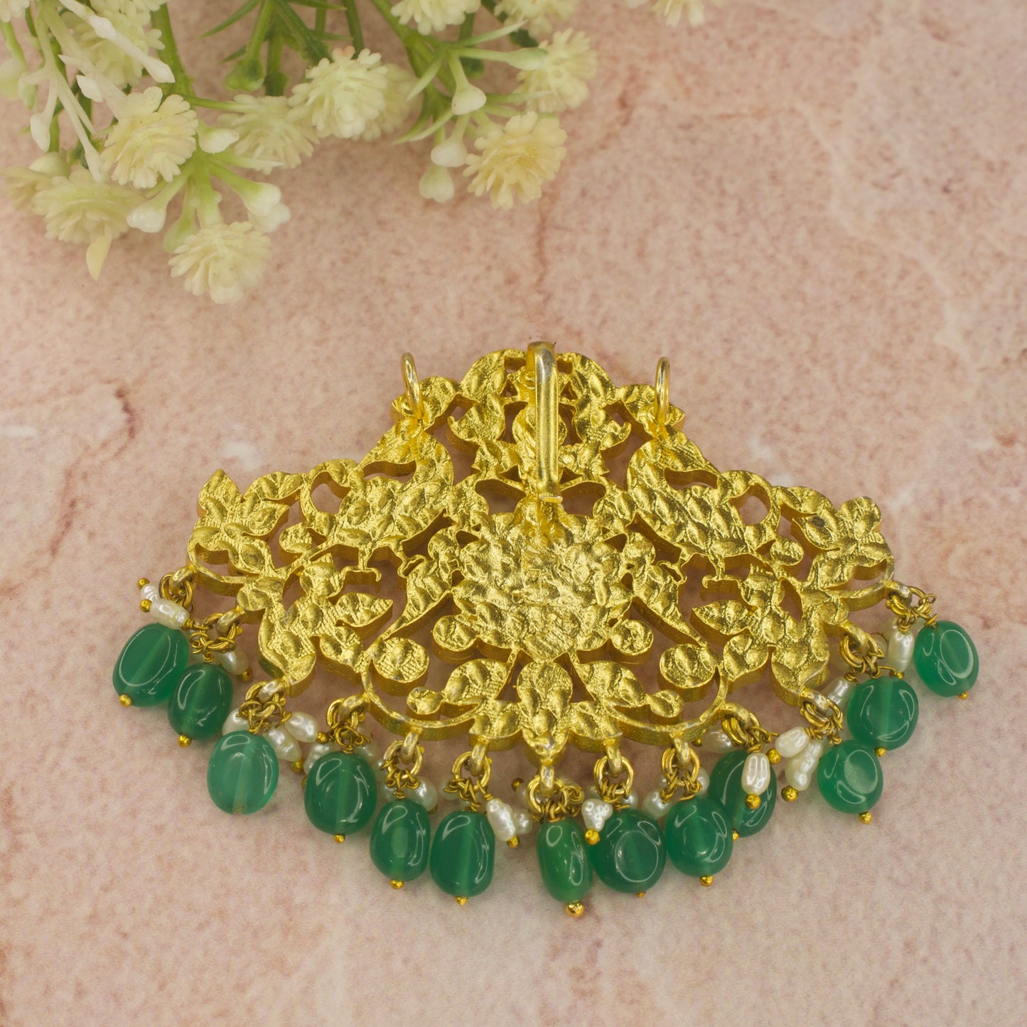 This is a Jadau Kundan pendant with Flower and peacock motifs . This pendant is covered in 22k Gold plating & at the bottom of the pendant we have ricepearls and green beads