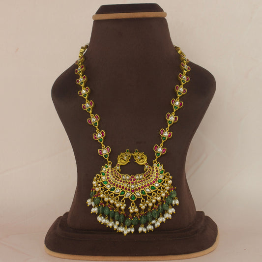This is a Jadau Kundan short necklace with pendant and side chain. The pendant has a little nakshi accent at top and the chain has flower design. The bottom of pendant has Russian emerald , small red beads and ricepearls.