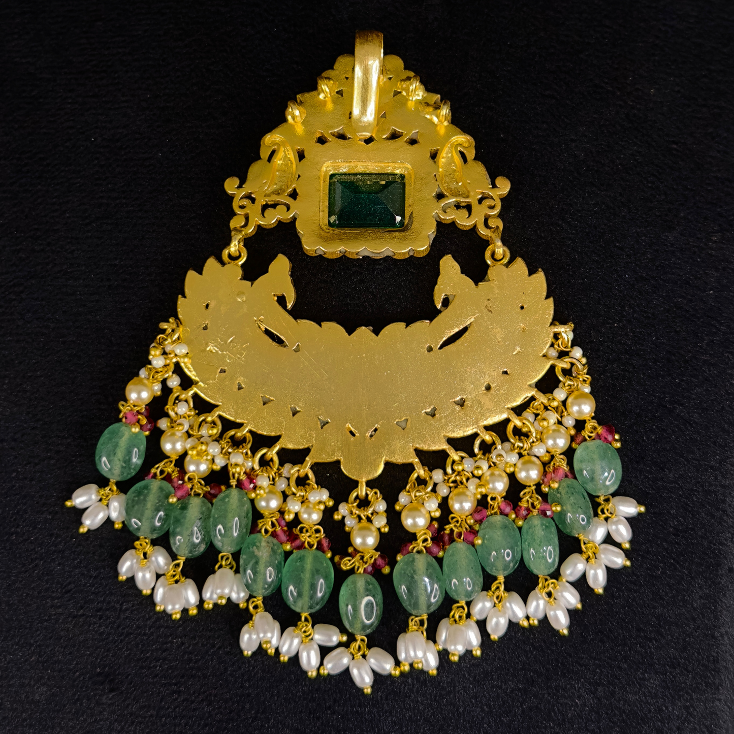 This is a jadau Kundan stone pendant with an emerald in middle. The pendant is large sized, it is covered with 22k Gold plating and at the bottom of the pendant we have strawberry beads and ricepearls