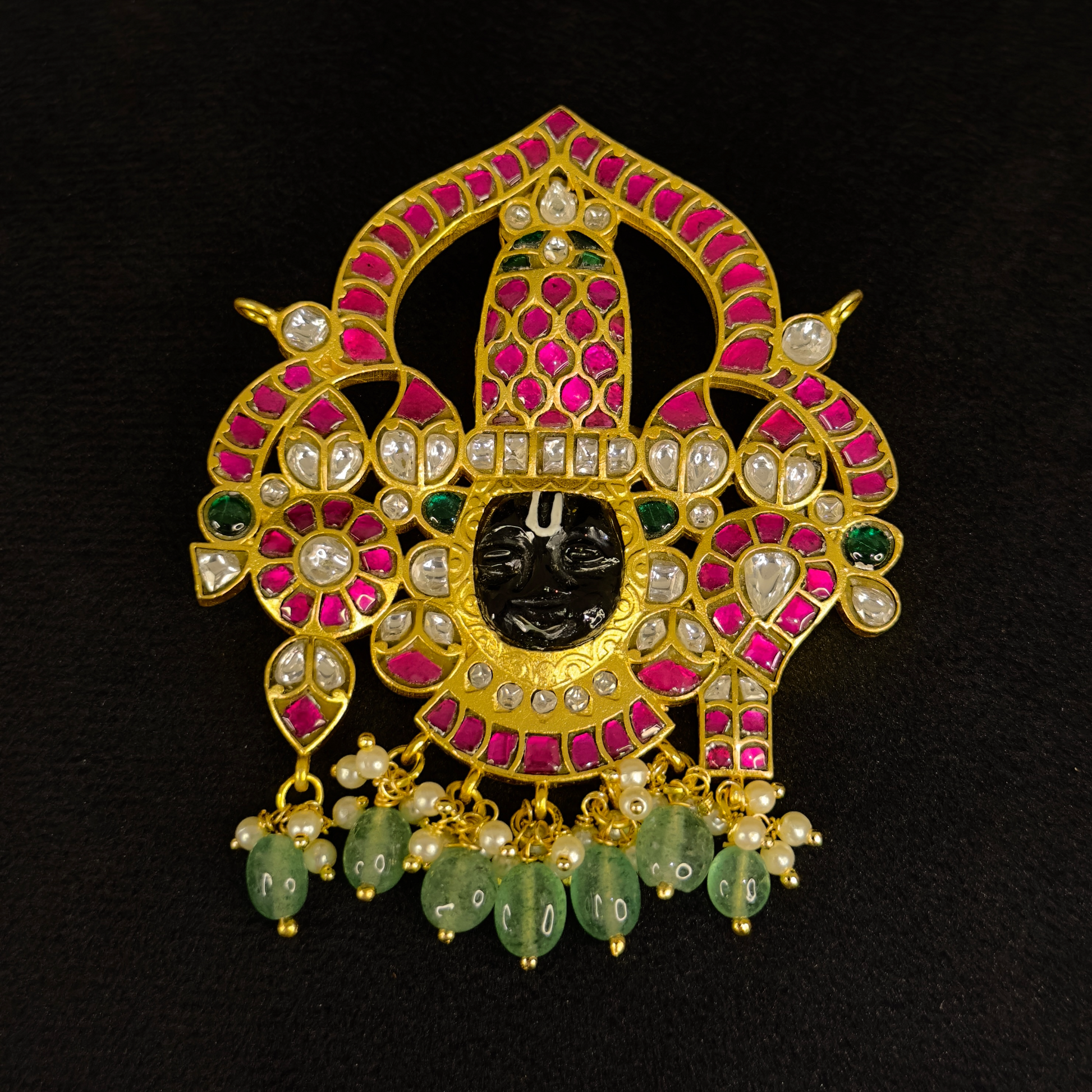 This is A Jadau Kundan pendant with Lord Balaji motif . This pendant is covered in 22k gold covering and at the bottom of the pendant there are Russian emeralds