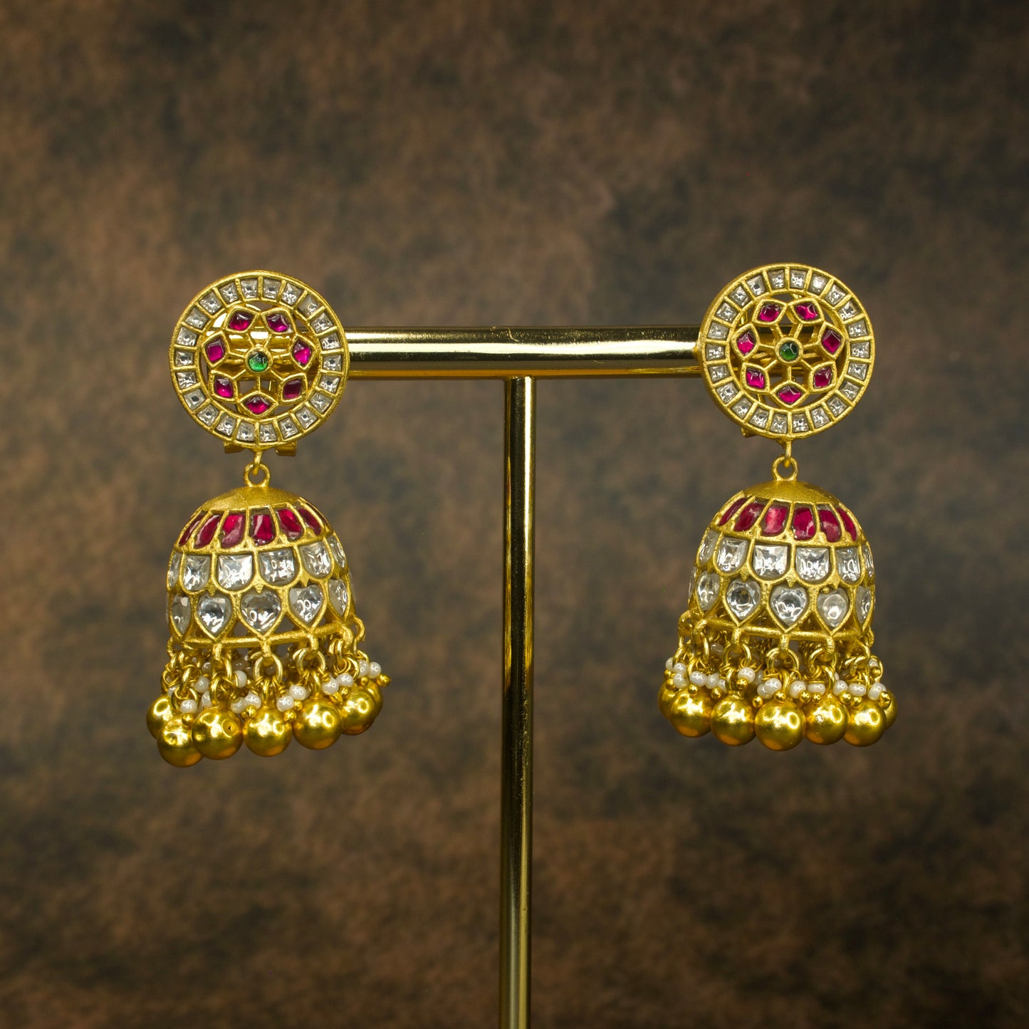 Jadau Kundan jhumkas with vibrant red and green gemstones, white Kundan stones, pearl drops, and gold beads, set in pure gold plating.