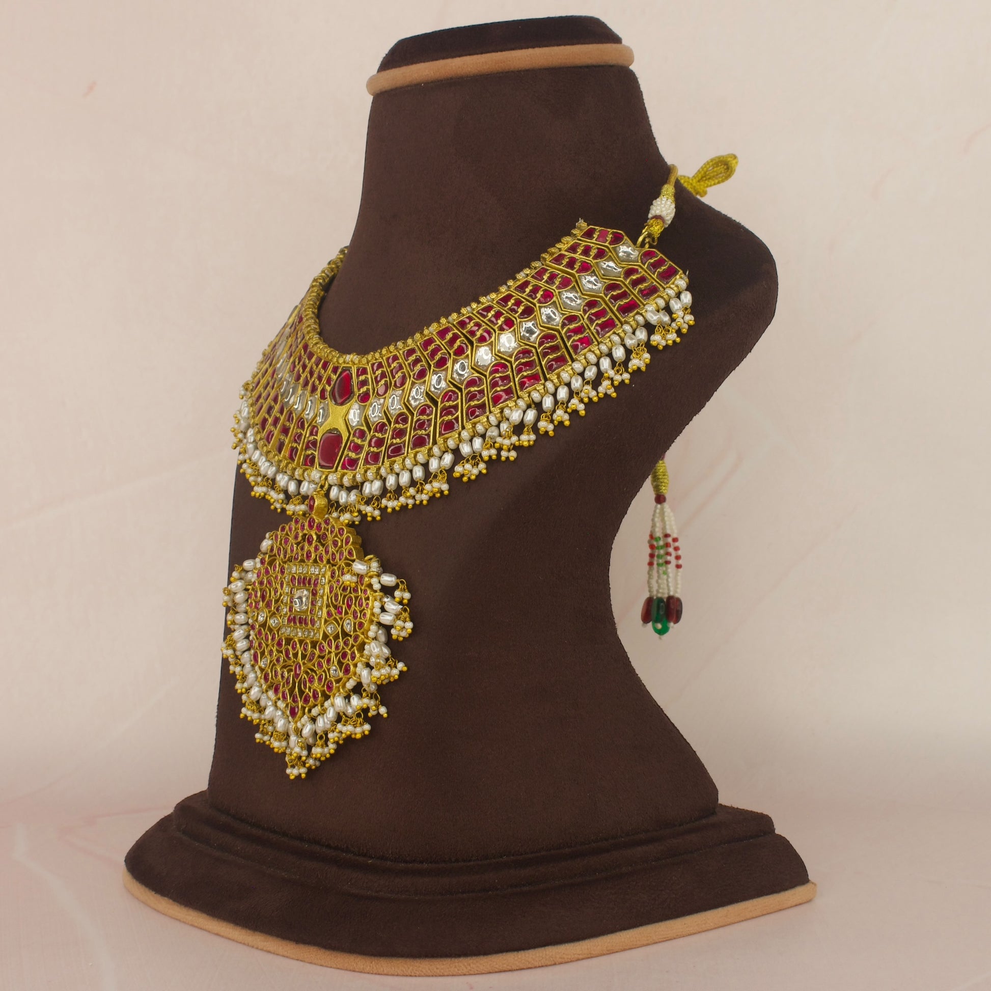 This is Jadau Kundan Short Necklace with red and white Kundan stones. This piece is covered in 22k Gold plating and at the bottom of this piece there are Ricepearls 