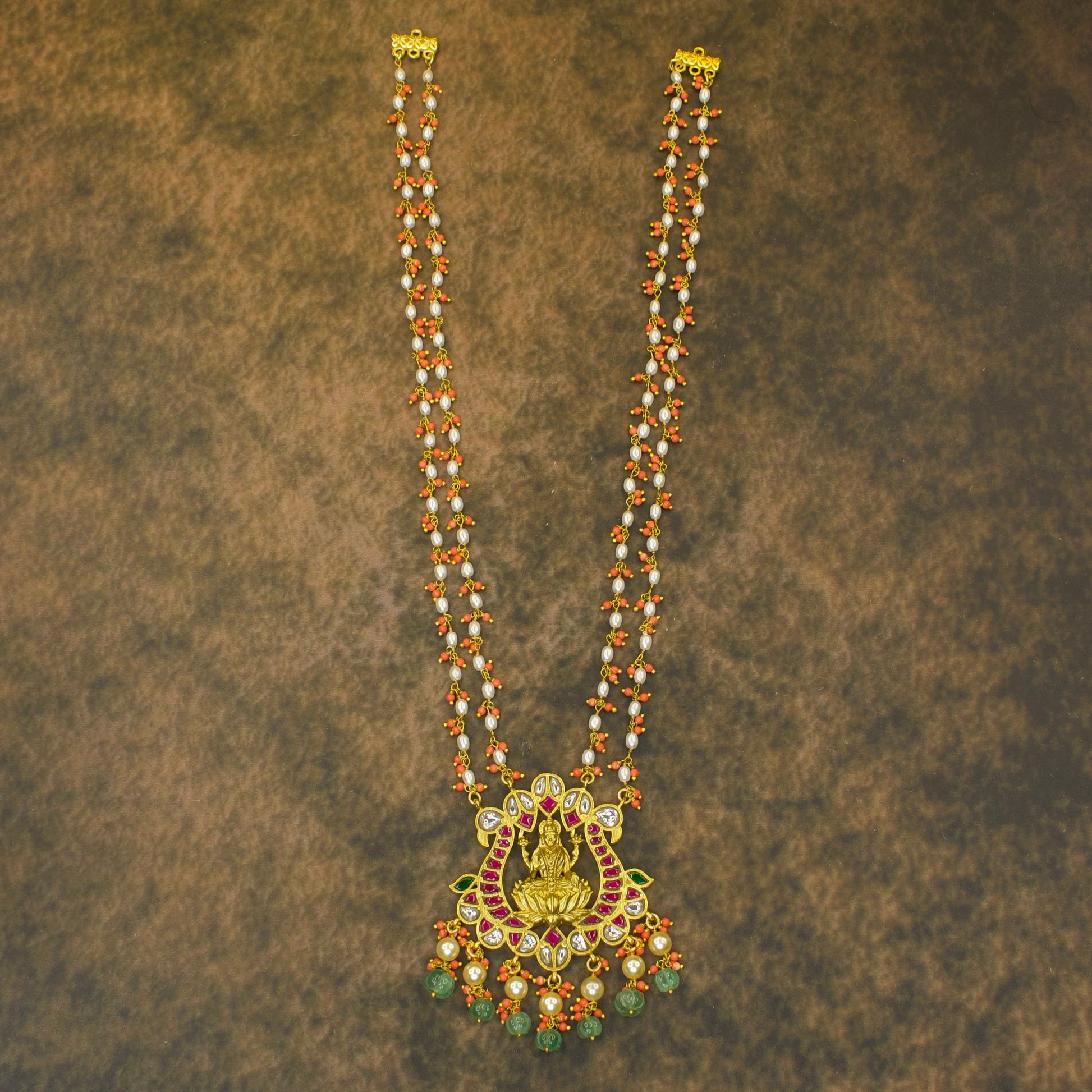 Elegant Laxmi Devi Jadau Kundan Pendant with coral beads. The necklace is studded with vibrant ruby and emerald gemstones. Apt for wedding, and other traditional ceremonies.