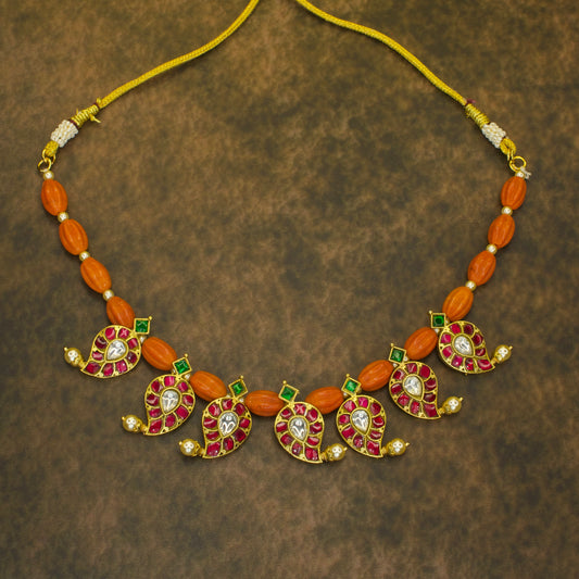 Jadau Kundan short necklace with coral beads and mango-shaped design, featuring Kundan stones set in gold with red and green gemstones.