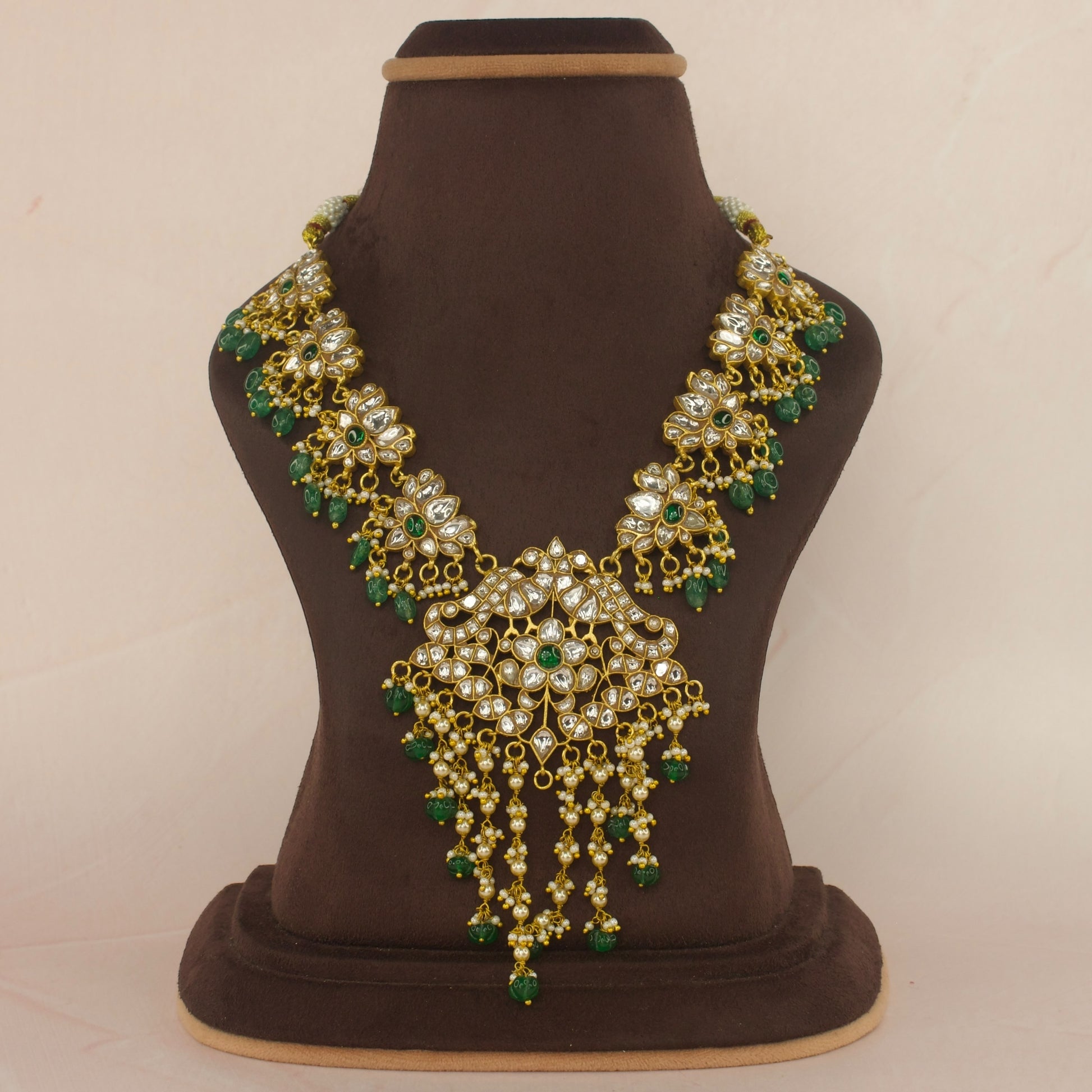 This is a Jadau Kundan Short Necklace, the Neckpiece has lotus designs all over it from the centre to the corners. This specific’s piece is with white Kundan stones and a singe green stone in the middle. The beads at bottom are Russian pumpkin beads.