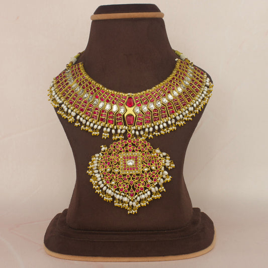 This is Jadau Kundan Short Necklace with red and white Kundan stones. This piece is covered in 22k Gold plating and at the bottom of this piece there are Ricepearls 
