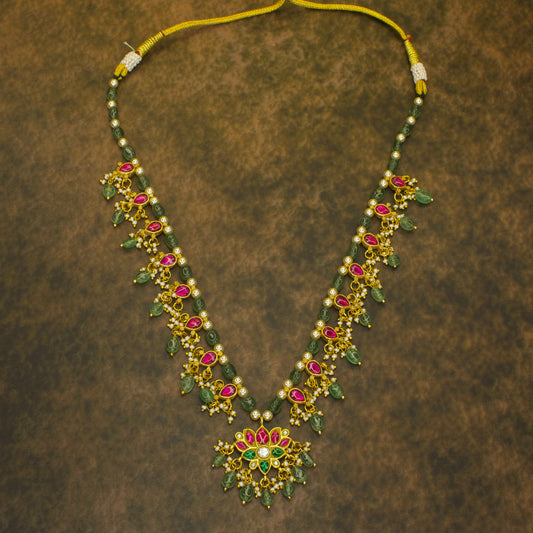 Jadau Kundan necklace with intricate red and green gemstone detailing, pearl and emerald bead drops, and a lotus motif centerpiece, set in pure 22k gold plating.