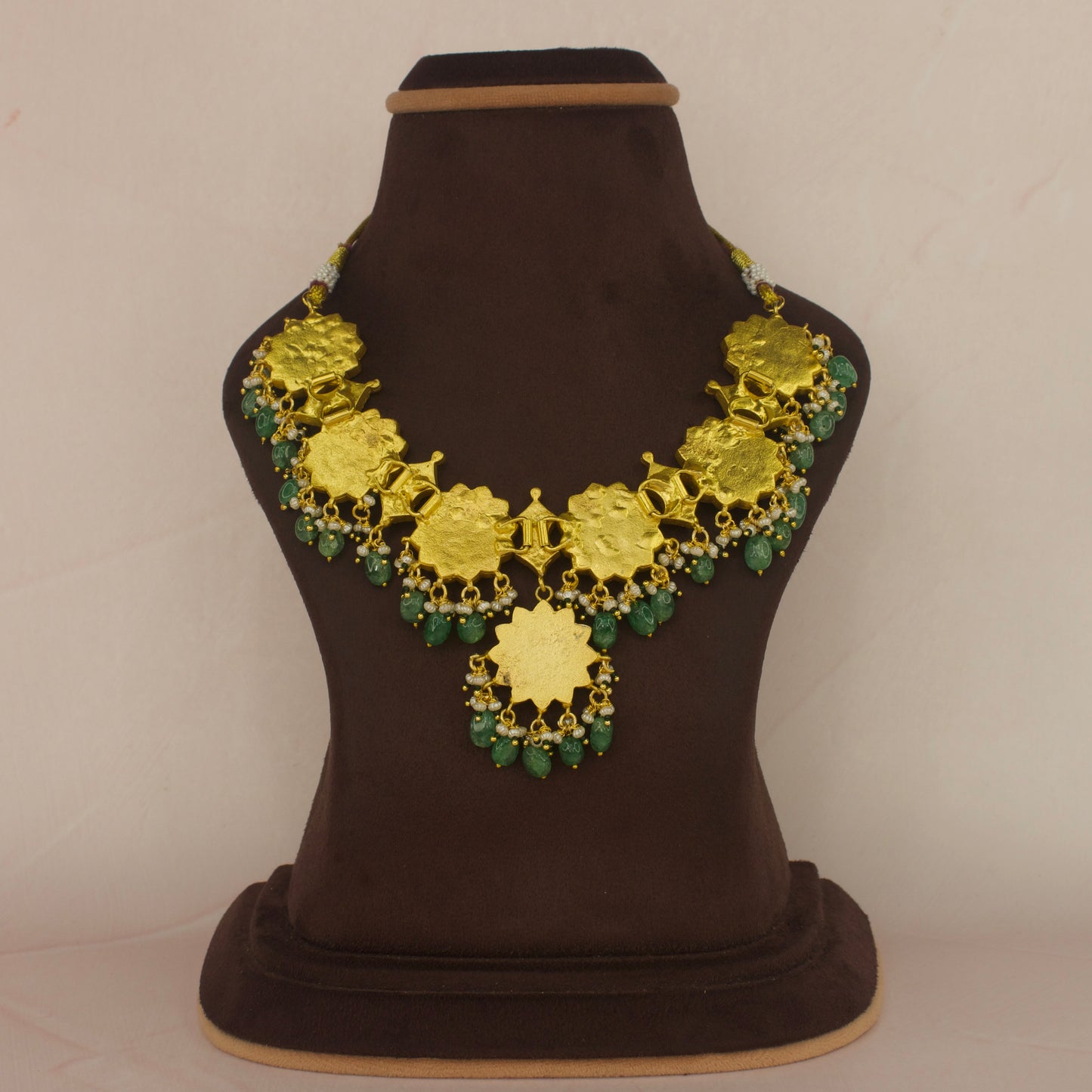 Here is A short Jadau Kundan bottumala necklace with floral design. This necklace has white Kundan stones and green stones in the middle of flowers. This piece is covered with 22k gold plating.