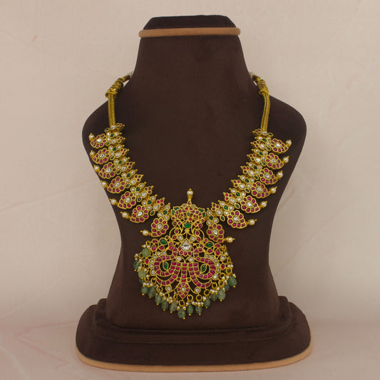 This is A jadau Kundan short necklace with mango and peacock motifs. This piece is covered with 22k gold plating and at the bottom of the pendant we have Russian beads